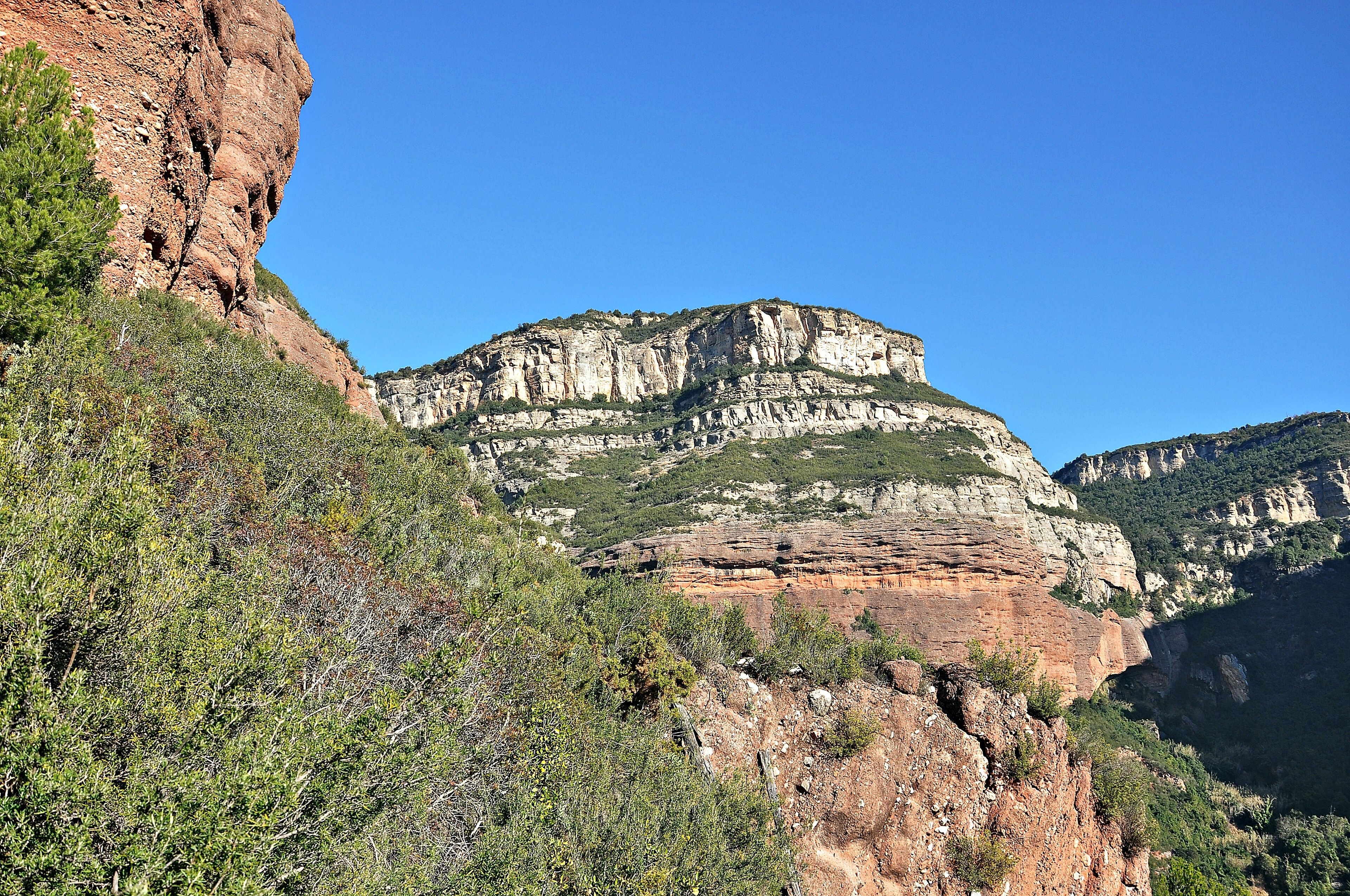 A rugged mountain landscape with layered rock formations and dense green vegetation.