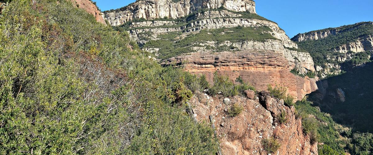 A rugged mountain landscape with layered rock formations and dense green vegetation.