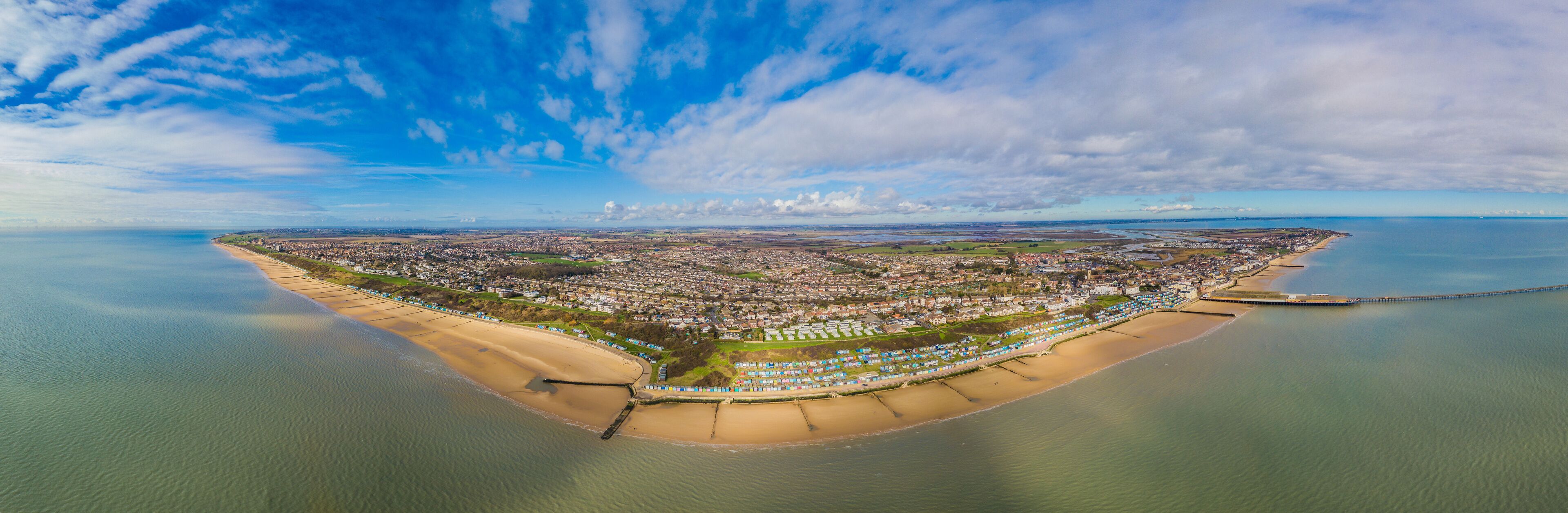 An aerial view of a coastal city with a beach, a pier, and a mix of residential and commercial buildings.
