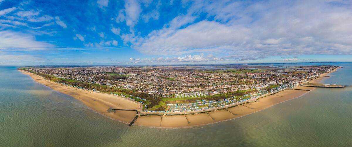 An aerial view of a coastal city with a beach, a pier, and a mix of residential and commercial buildings.