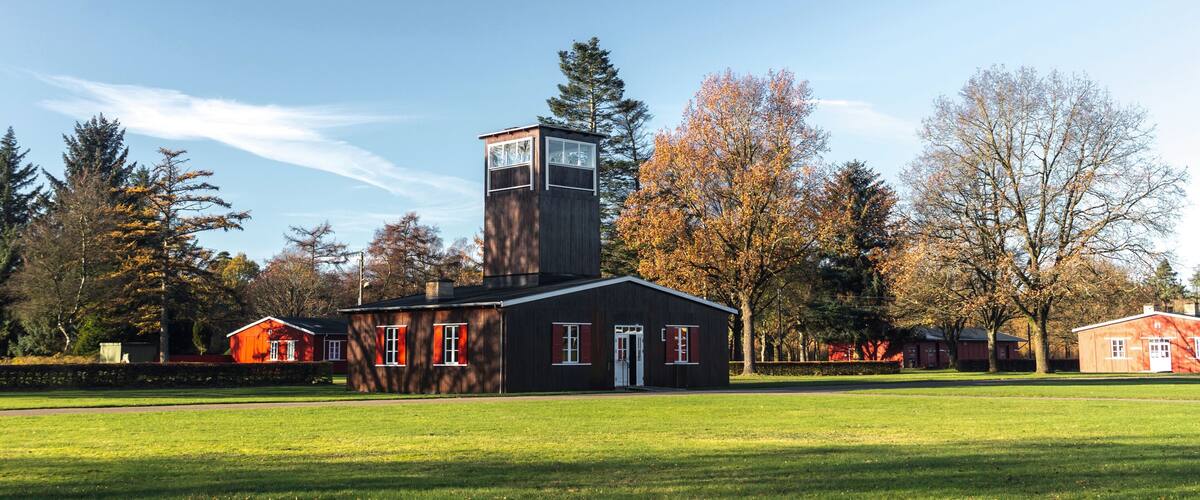 A modern building with a tower, surrounded by a grassy field and autumn-colored trees.