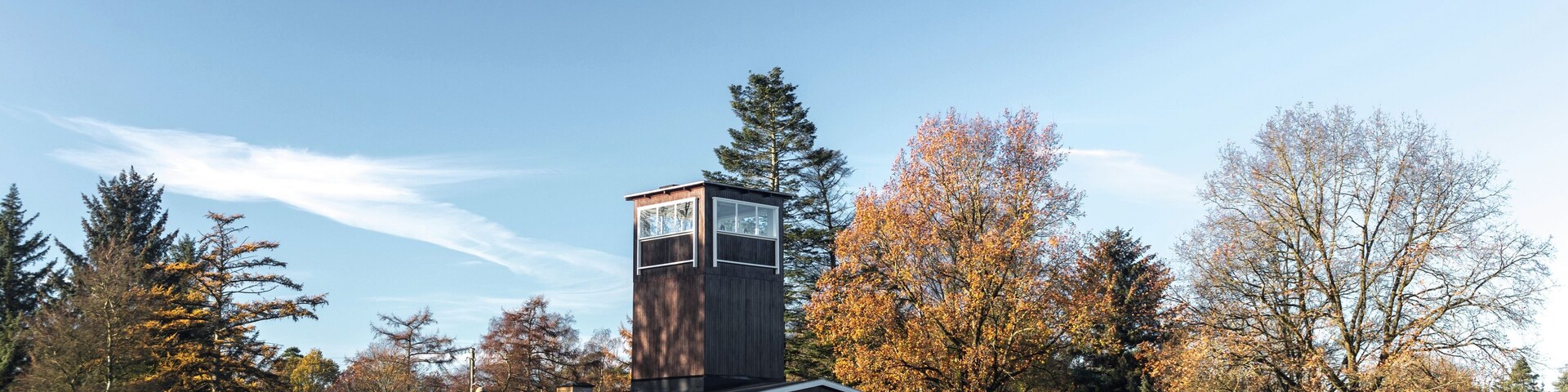 A modern building with a tower, surrounded by a grassy field and autumn-colored trees.