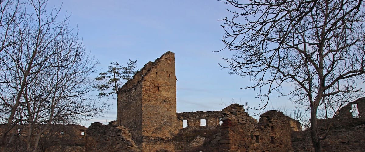 A historical stone ruin with a tall central tower, surrounded by trees and other ruins.