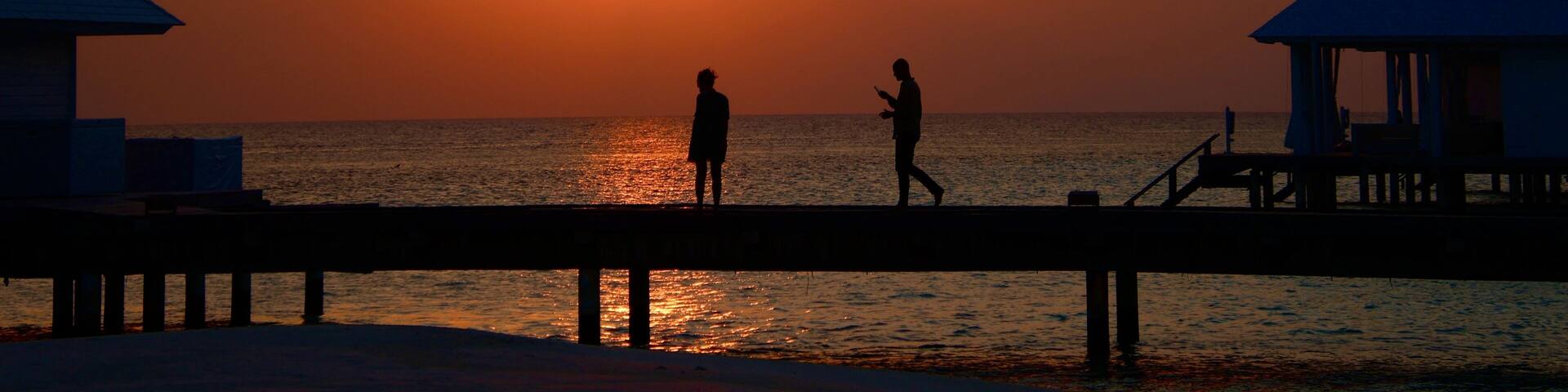 sunset on the wooden pier at a Maldives island with people silhouette