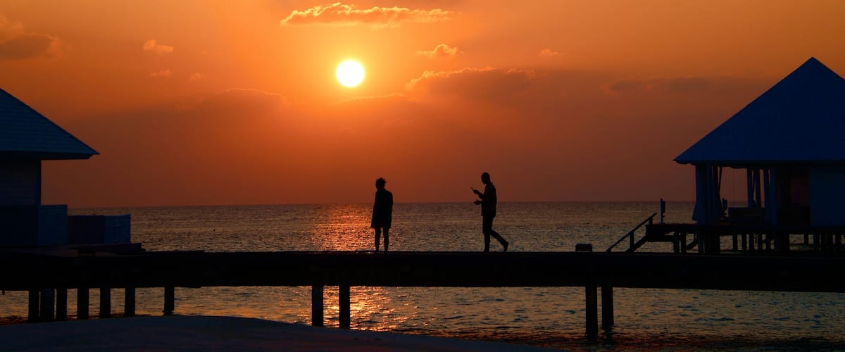 A sunset over the ocean with two people walking on a pier.
