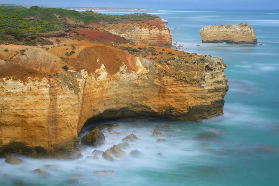 A coastal landscape with layered rock formations and a calm sea.