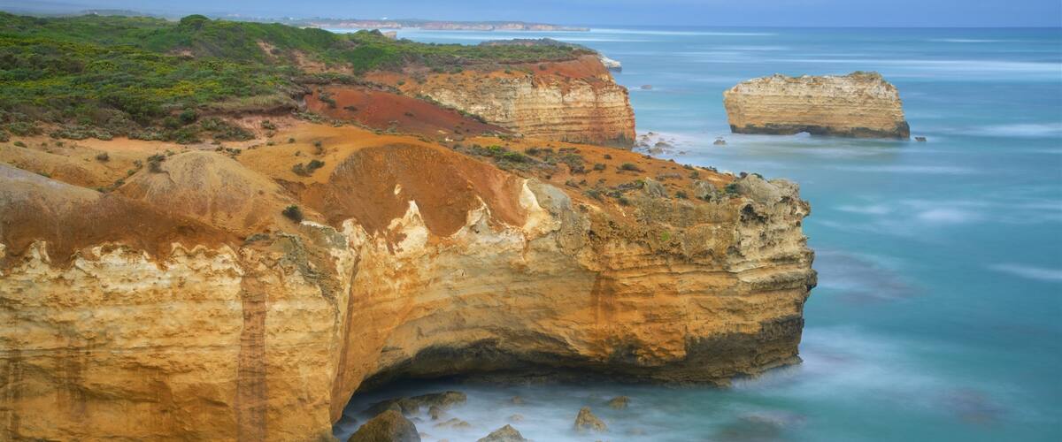 A coastal landscape with layered rock formations and a calm sea.