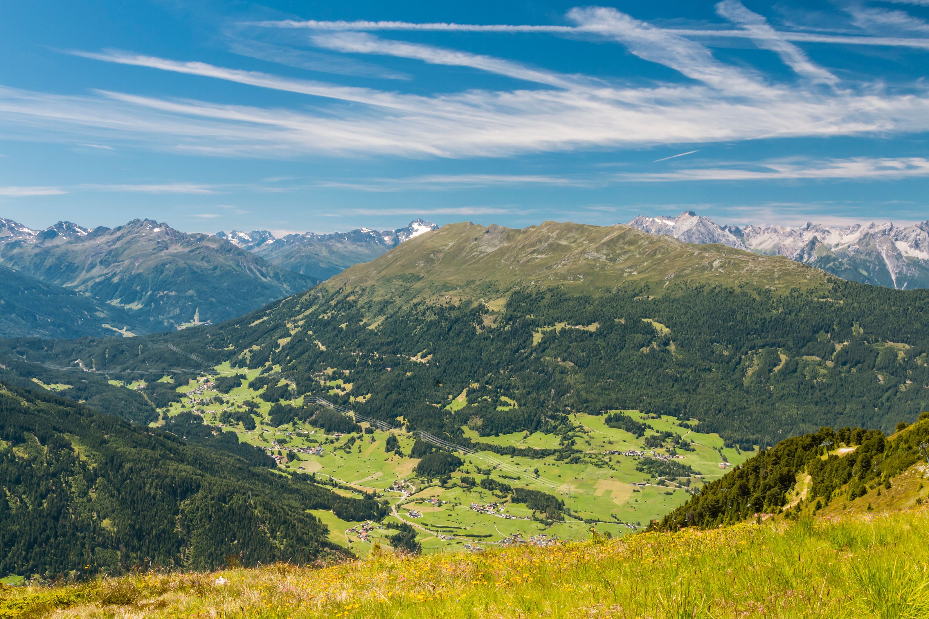 A mountainous landscape with a valley, scattered houses, and a clear blue sky.