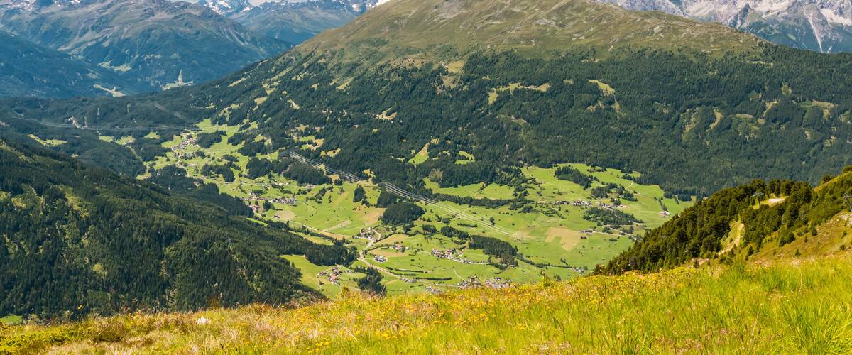 A mountainous landscape with a valley, scattered houses, and a clear blue sky.