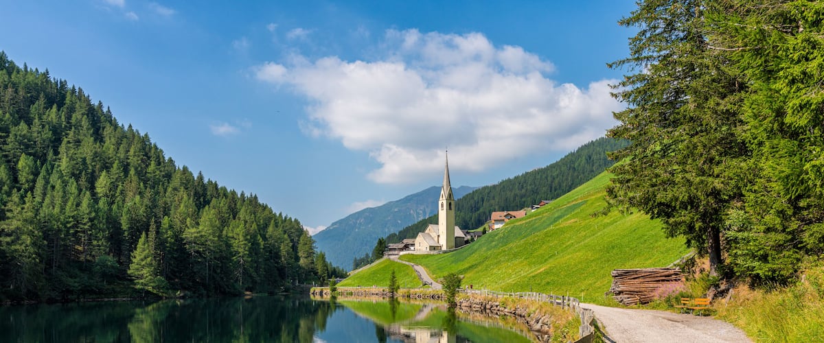 A serene lake with a church, surrounded by lush green hills and a clear blue sky.