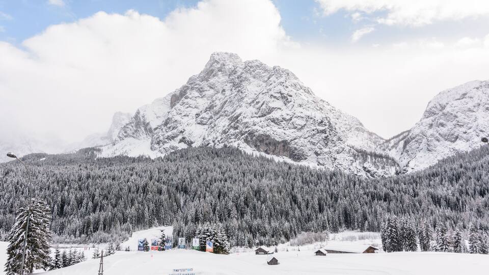 A snow-covered mountain range with dense forests and wooden cabins.
