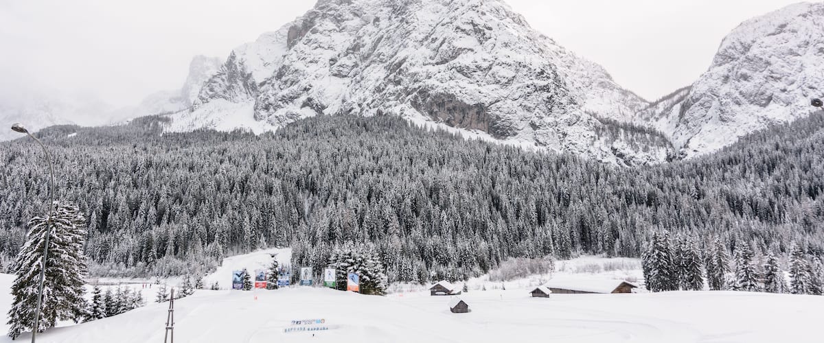 A snow-covered mountain range with dense forests and wooden cabins.