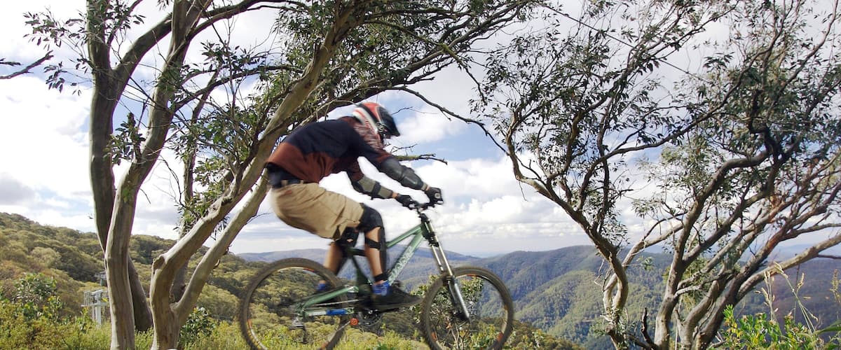A mountain biker performing a jump over a rocky terrain with a mountainous landscape in the background.