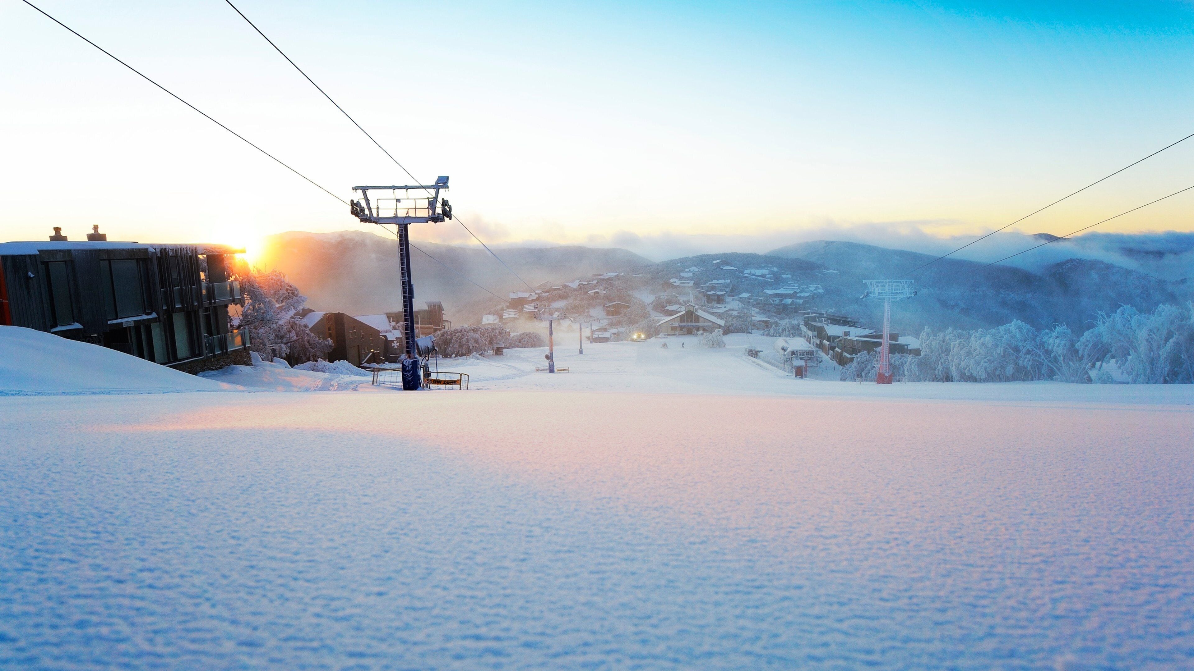 A snowy ski resort with a ski lift, buildings, and a mountain backdrop.