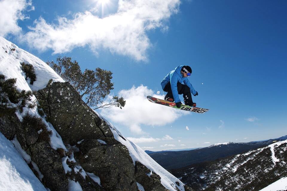 A snowboarder mid-air performing a jump on a snowy mountain slope.