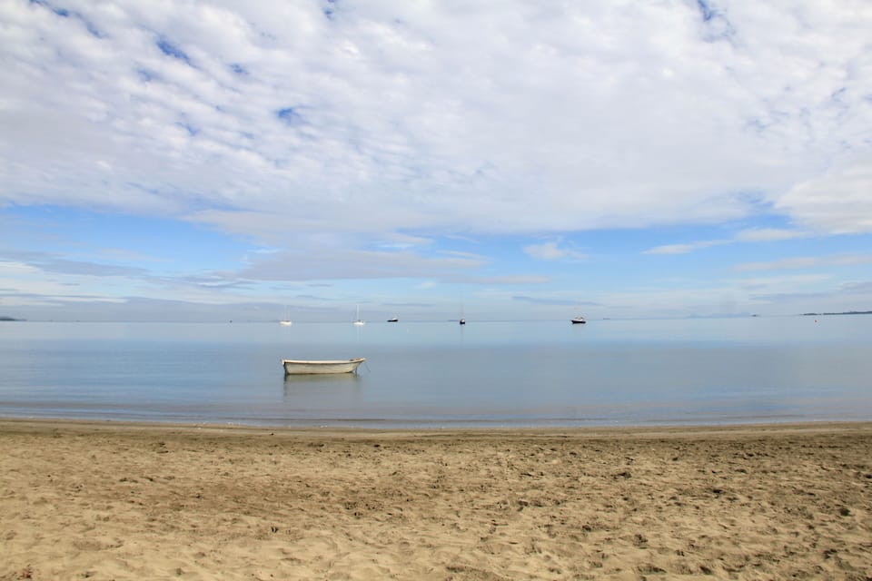 A calm beach with a small boat anchored in the water and a clear sky above.