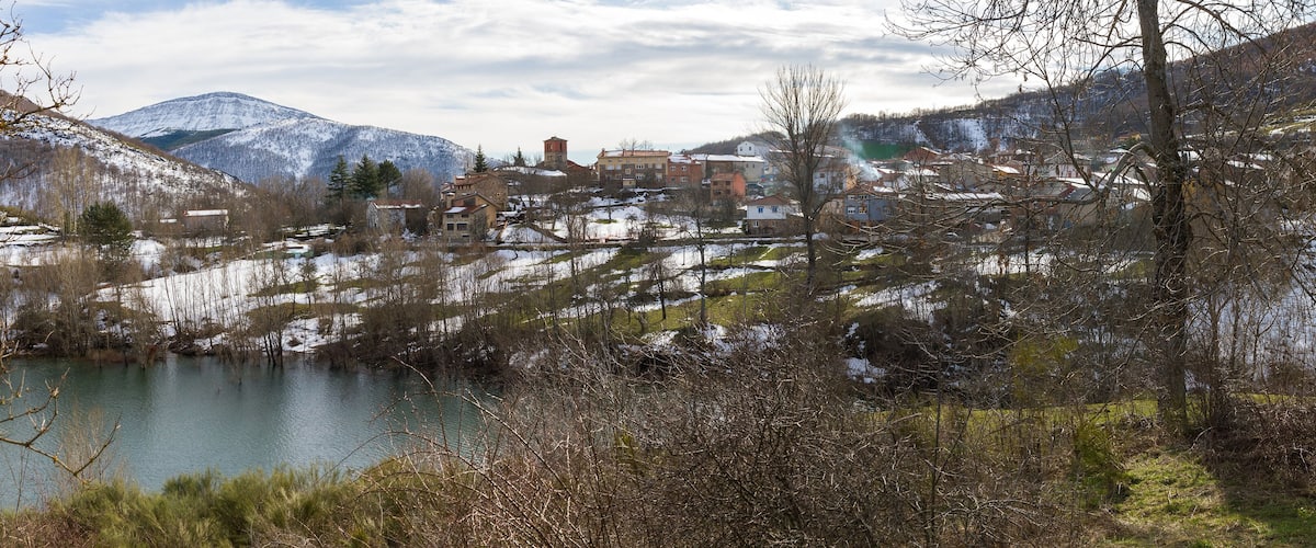 A mountainous landscape with a lake, snow-covered hills, and a town with historic buildings.