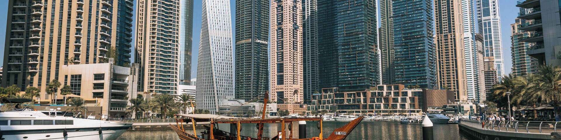 A modern cityscape with high-rise buildings and a traditional boat docked at a marina.
