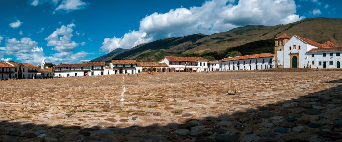 A cobblestone plaza with white buildings and a mountain in the background.