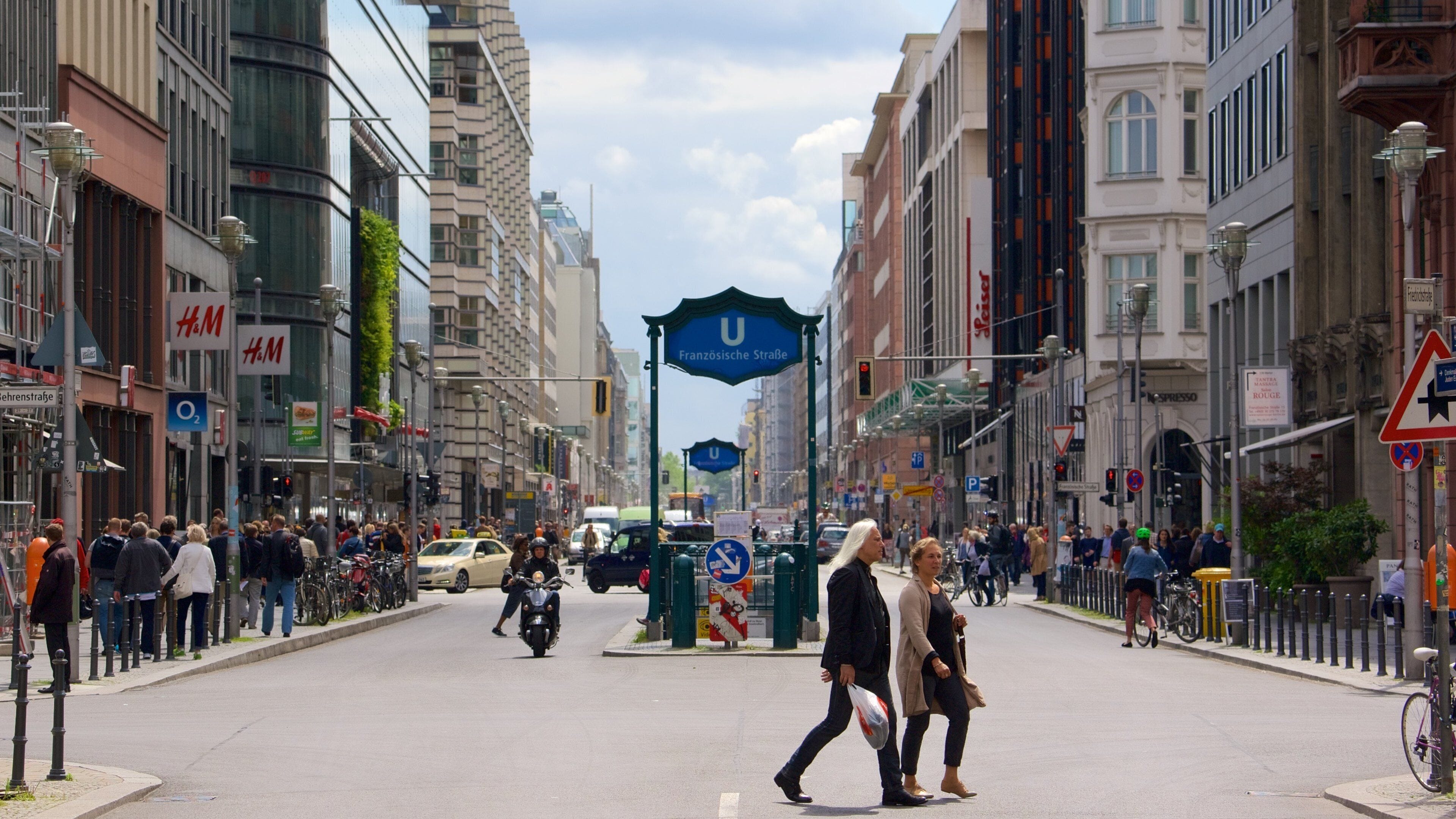 A busy urban street with pedestrians, cyclists, and vehicles.