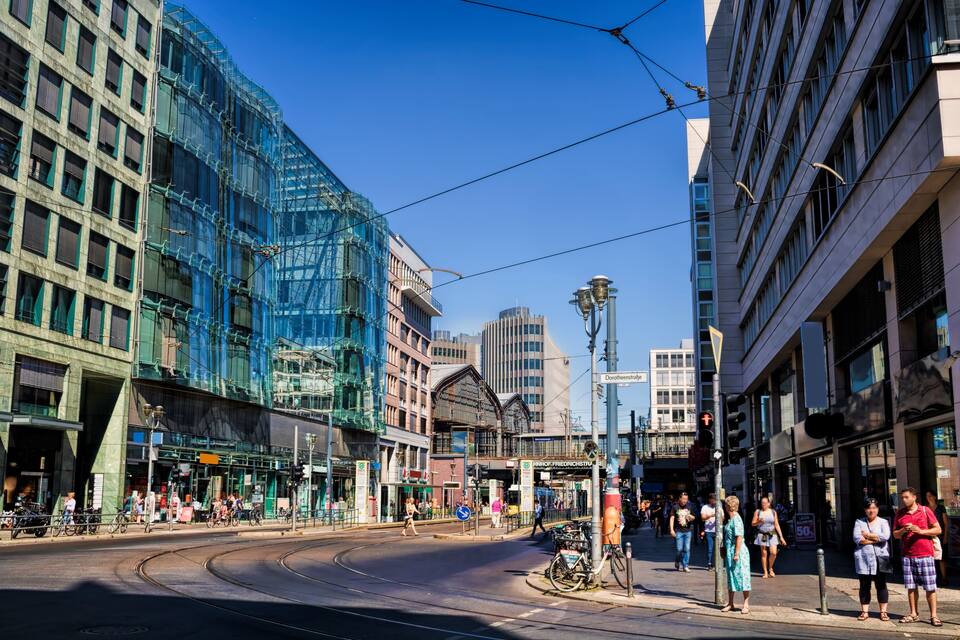 A city street with tram tracks, modern buildings, and pedestrians.