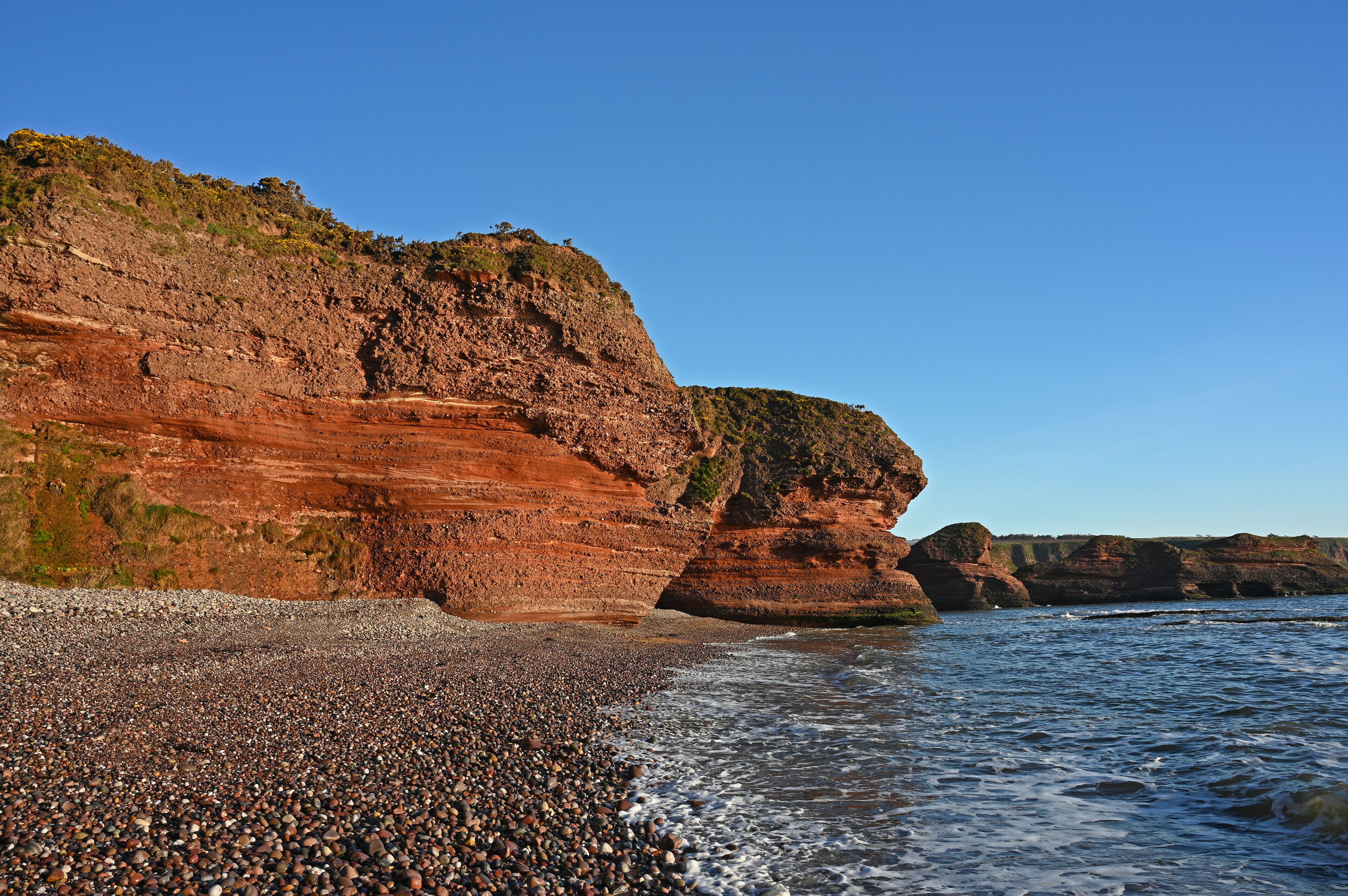 A rocky coastline with layered cliffs and pebbly beach.