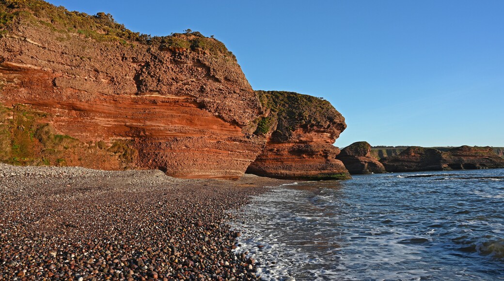 A rocky coastline with layered cliffs and pebbly beach.