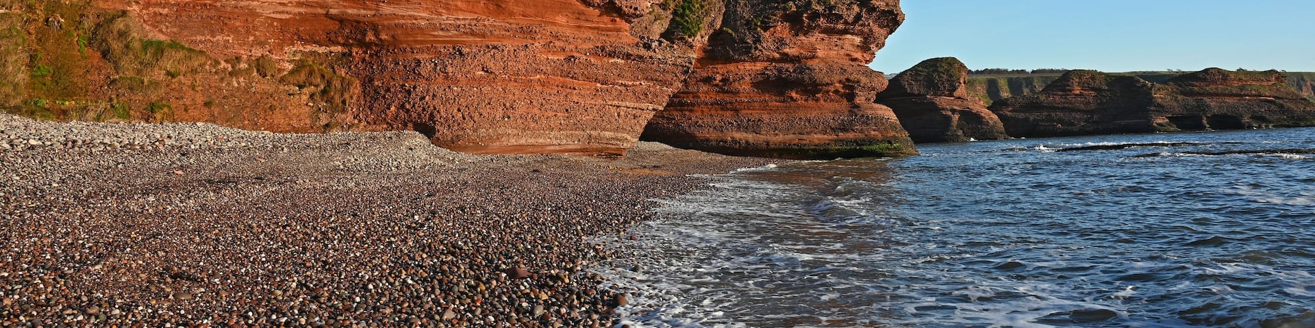 A rocky coastline with layered cliffs and pebbly beach.