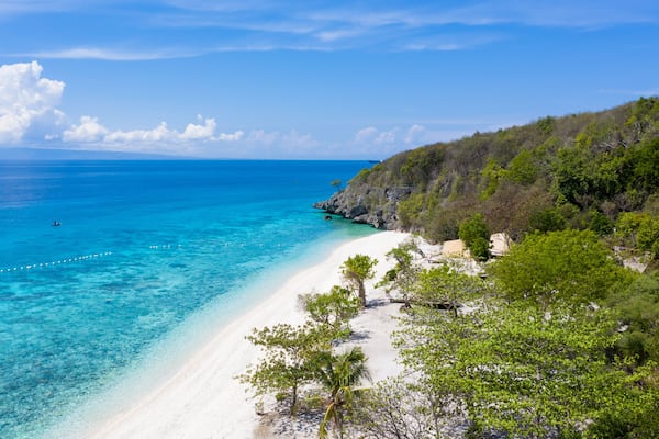 Une plage à l’eau turquoise et limpide, au sable blanc et bordée d’une végétation verdoyante.