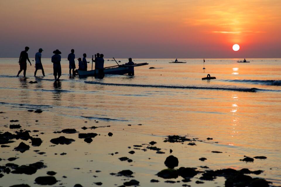 A sunset over a beach with people and boats.