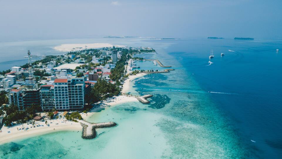 An aerial view of a coastal town with a beach, clear blue waters, and boats.