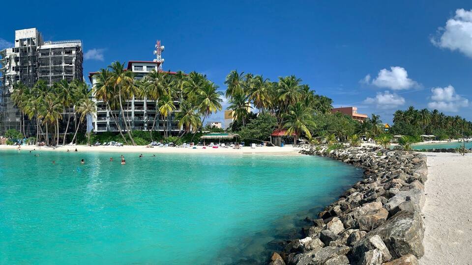 A beach with clear turquoise water, a rocky breakwater, and a building under construction.
