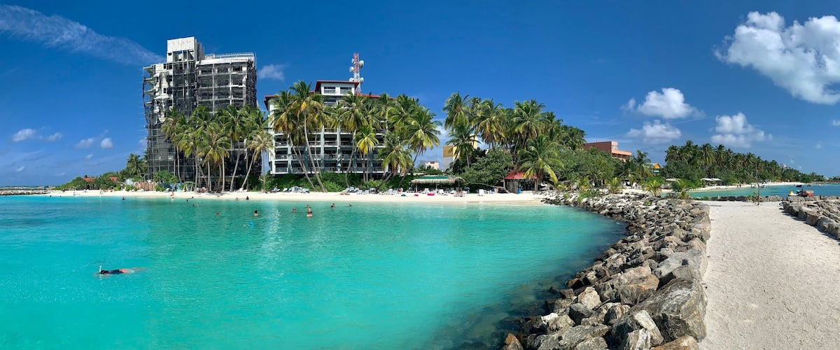 A beach with clear turquoise water, a rocky breakwater, and a building under construction.