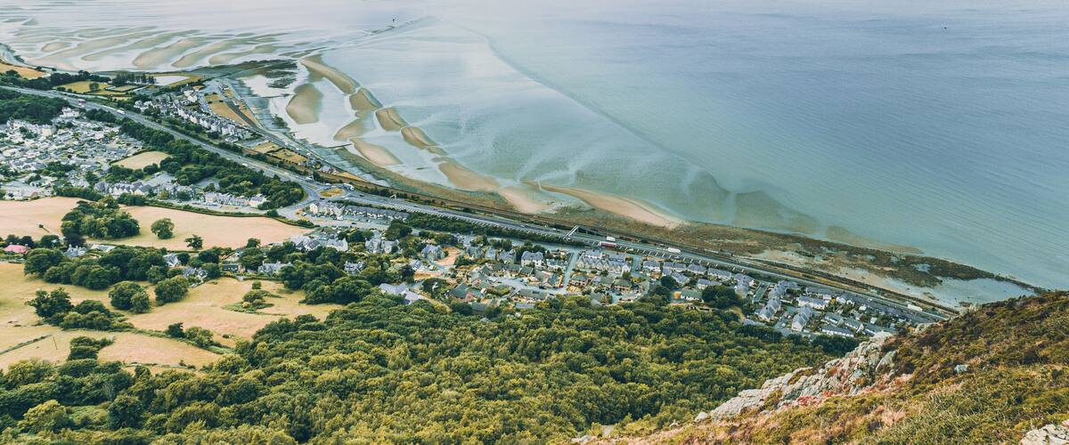 A coastal town with a beach, a bridge, and a forested hill.