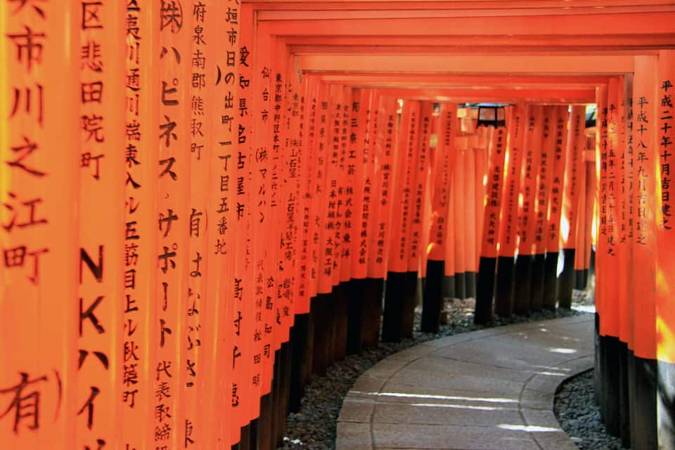 Un sendero flanqueado por torii de color naranja con inscripciones japonesas.