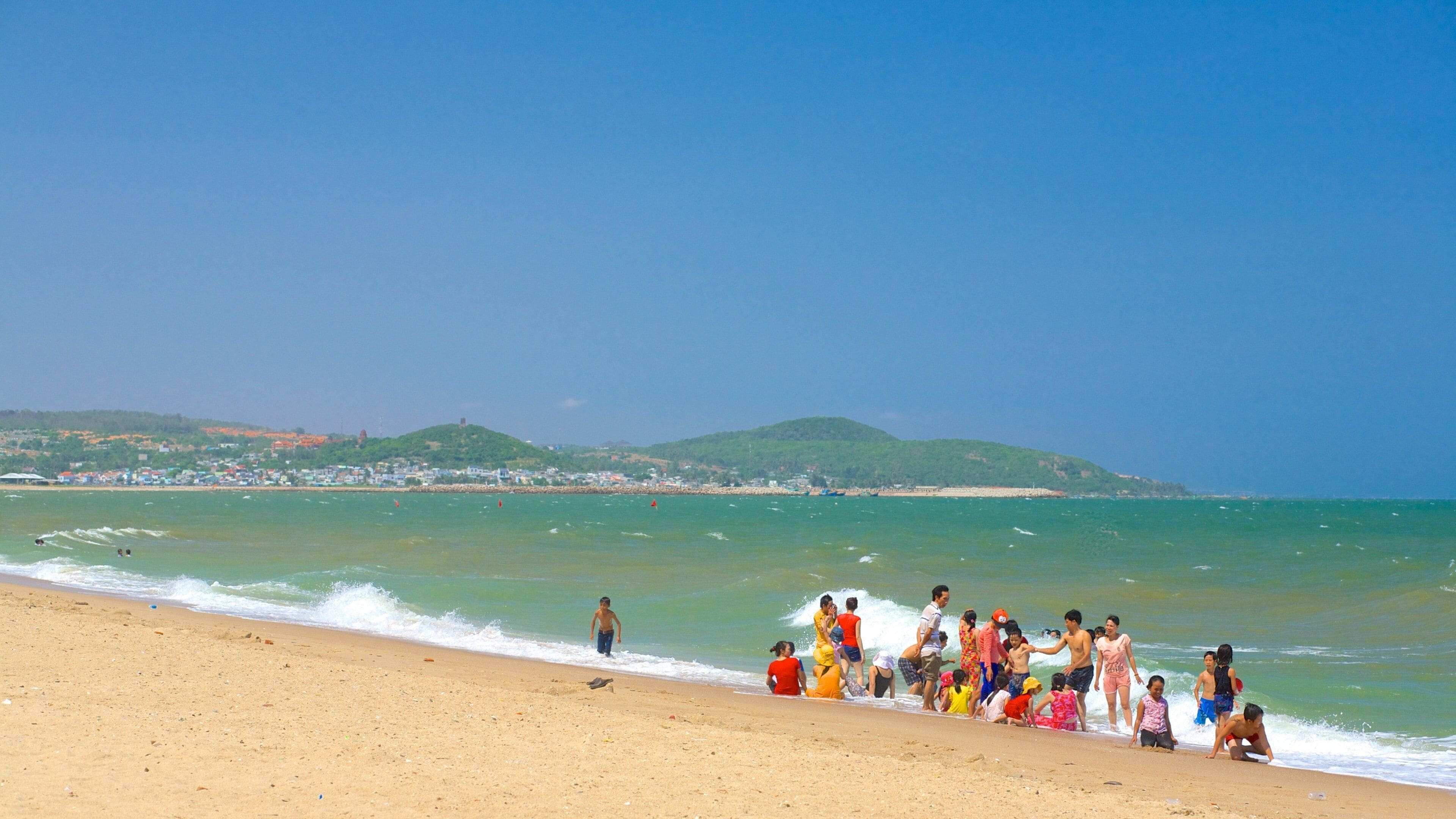 Une plage où l’on voit des gens dans l’eau et sur le rivage.