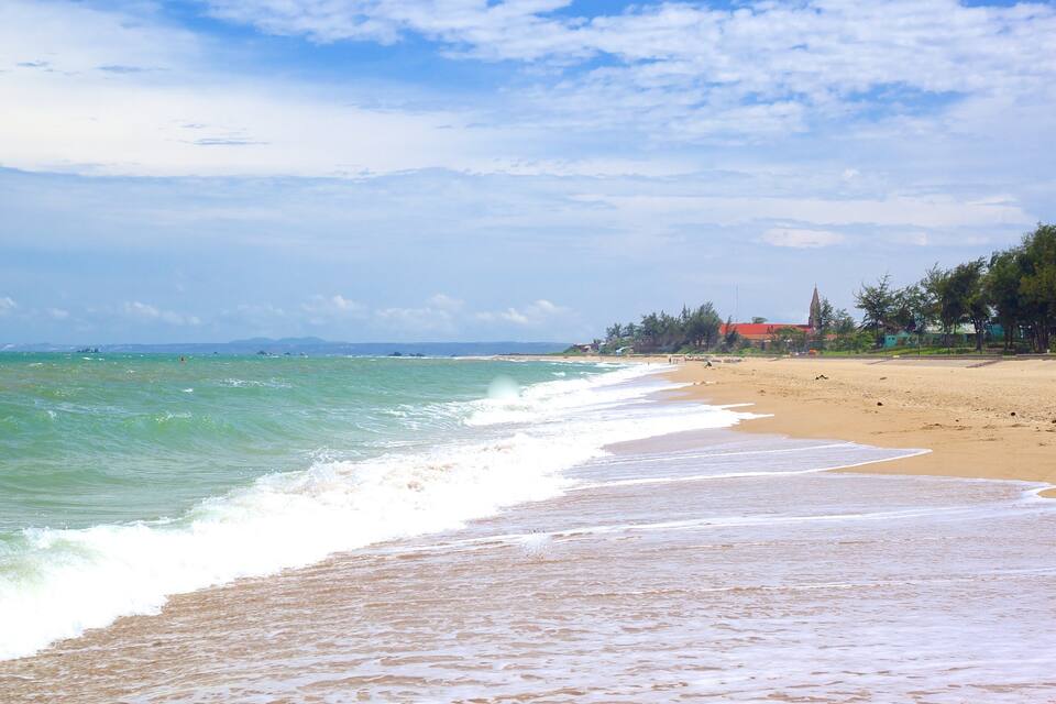 A beach with waves, a clear sky, and distant mountains.