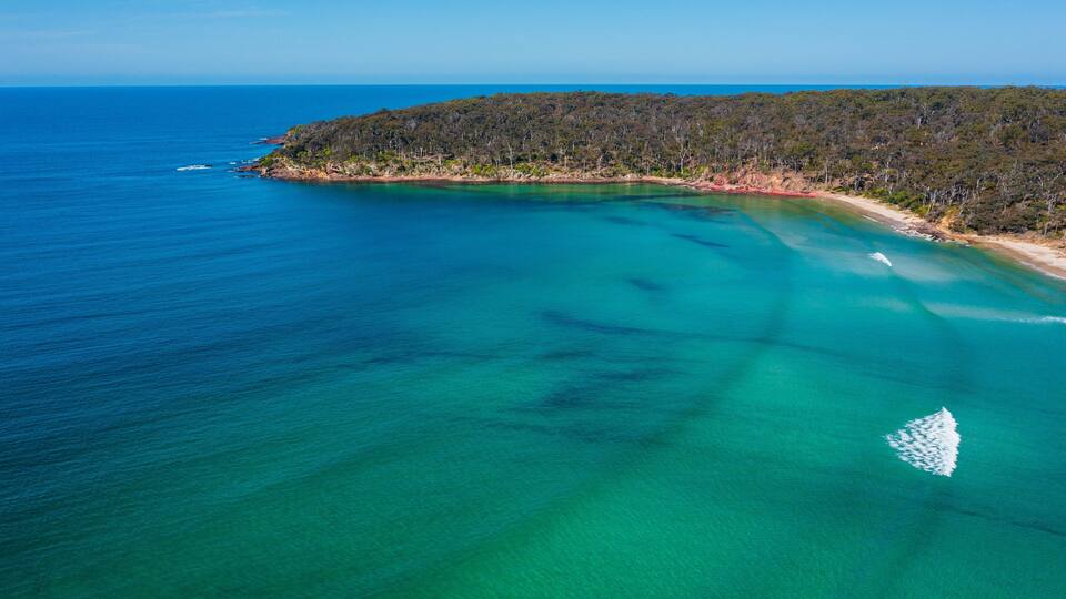 A coastal landscape with clear turquoise waters, a sandy beach, and a forested island.