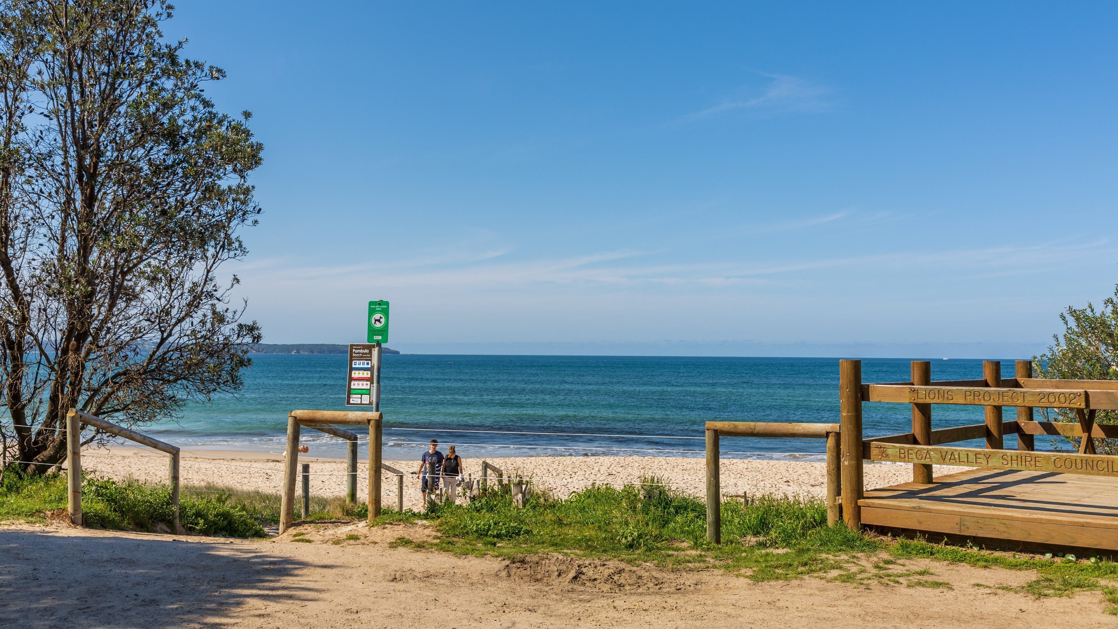 A beach with a wooden boardwalk, a signpost, and a clear view of the ocean.
