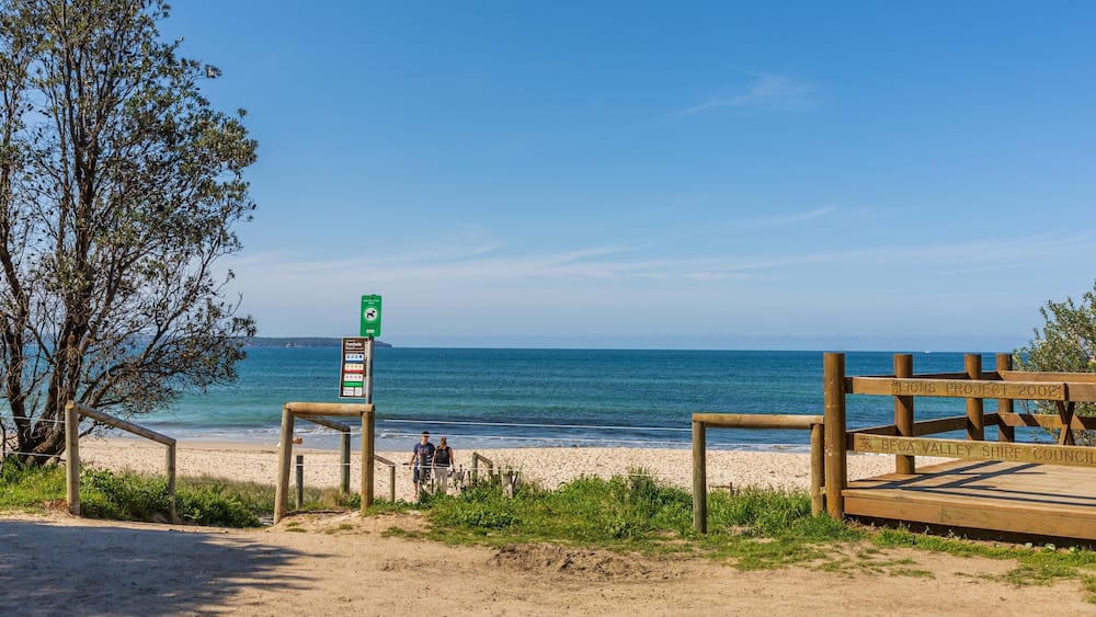Une plage avec une promenade en bois, un panneau indicateur et une vue dégagée sur l’océan.