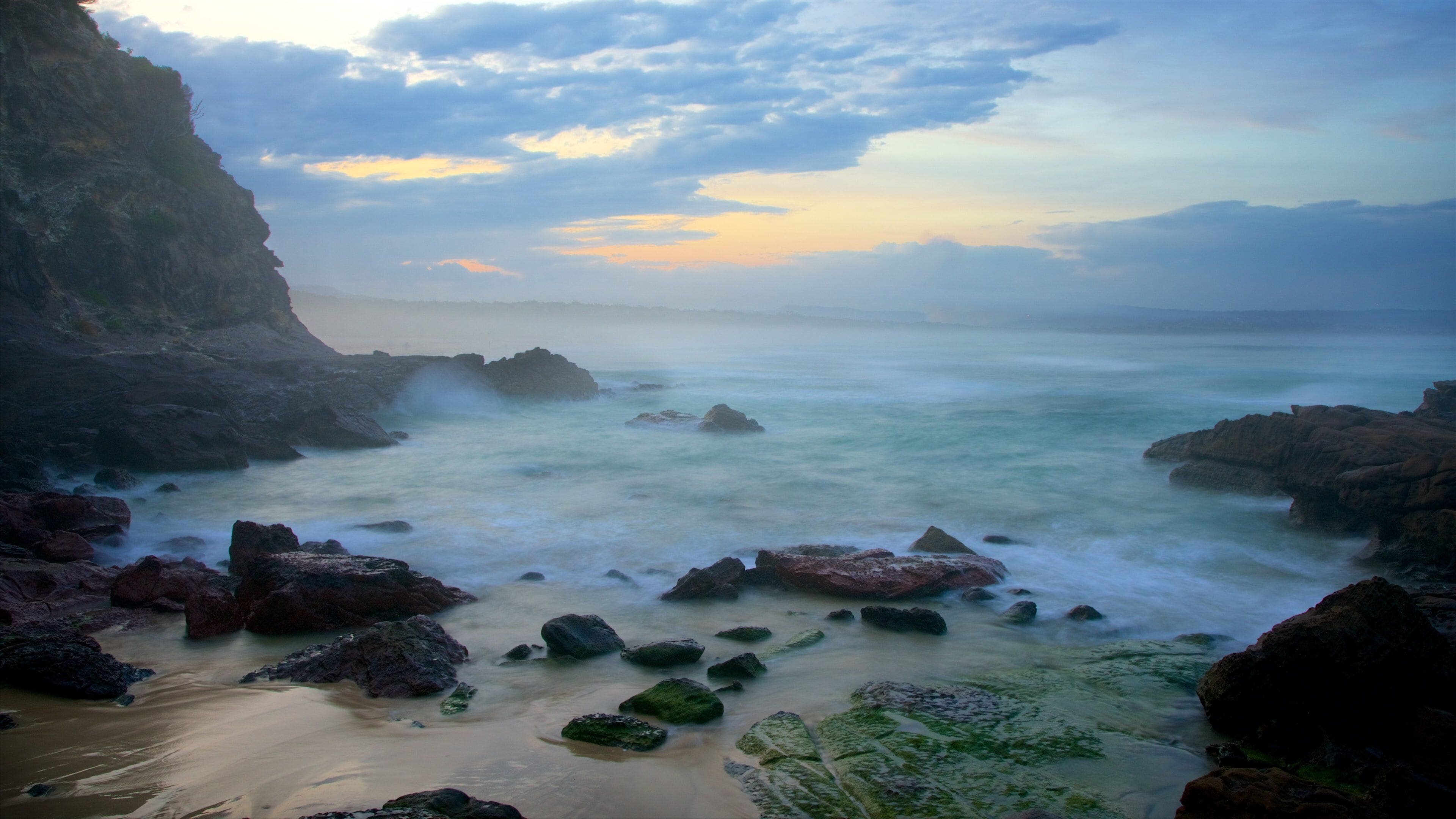 A coastal landscape with rocky shores, calm sea, and a cloudy sky.
