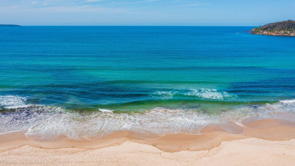 A beach with clear blue water and a sandy shore.