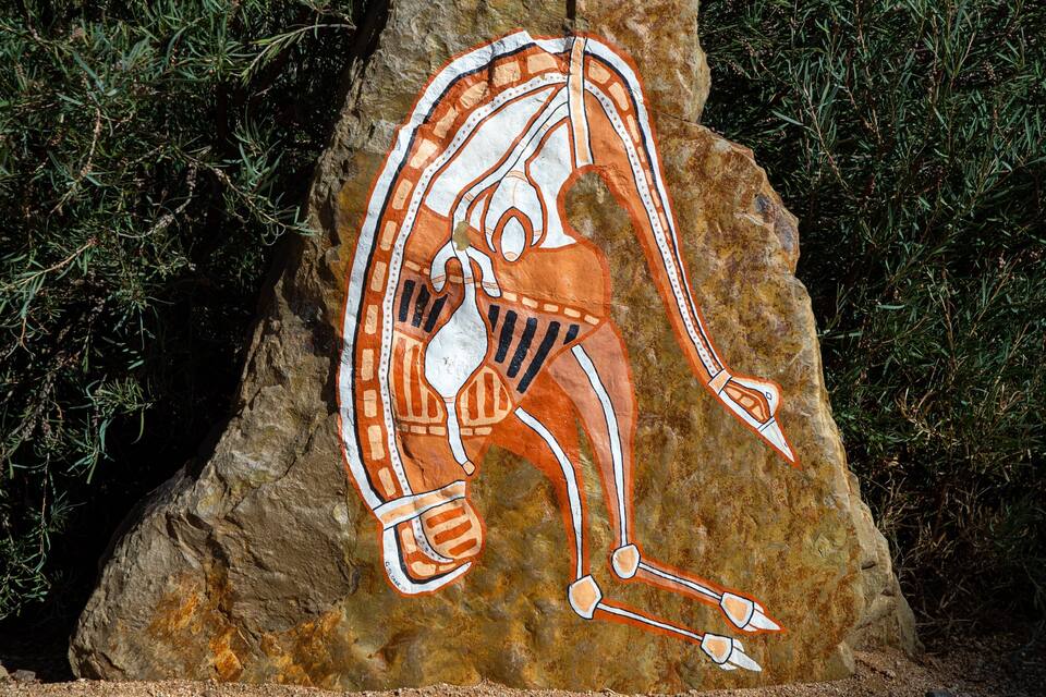 Ein Felsen mit einer Malerei, die eine sich bewegende Figur zeigt, umgeben von Grünpflanzen.
