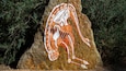 A rock with a painted depiction of a figure in motion, surrounded by greenery.