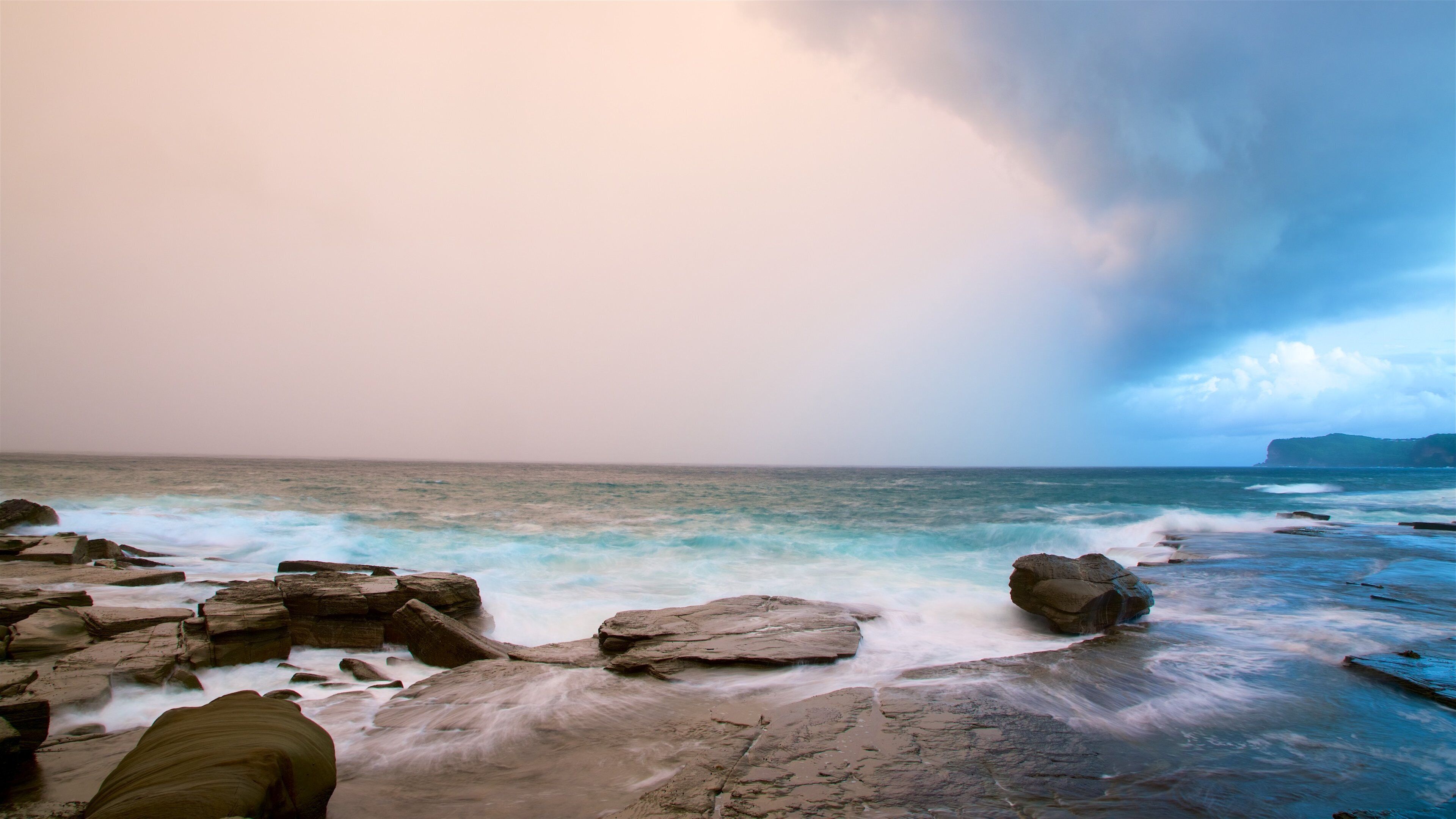 A rocky shoreline with waves crashing against the rocks under a cloudy sky.