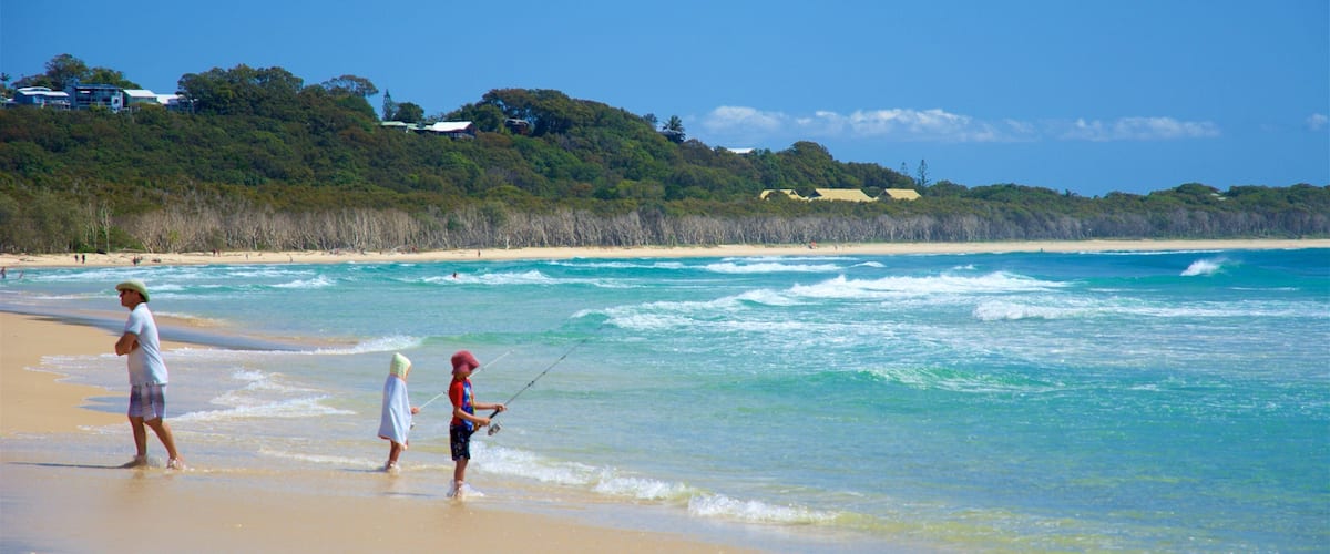 A beach with clear turquoise waters, a sandy shore, and a forested hill in the background.