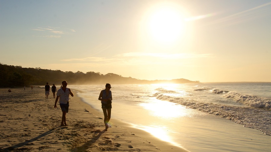 Una playa con gente caminando por la orilla durante el atardecer.