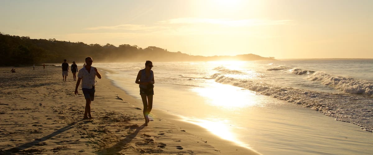 A beach with people walking along the shore during sunset.