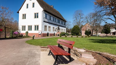 A white building with green shutters, a stone bench, and a well-maintained lawn.