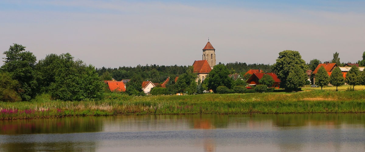 A calm lake with a church and houses in the background.